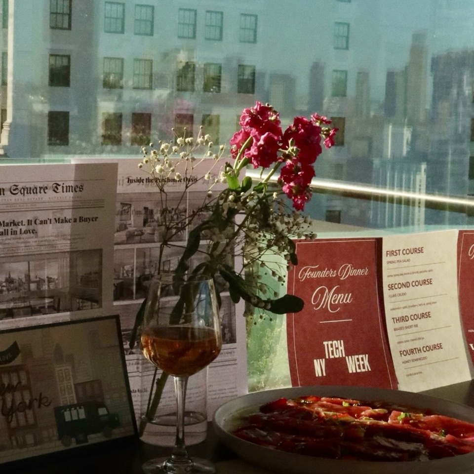 A dinner table set with flowers, wine and a NY Tech Week founders dinner menu